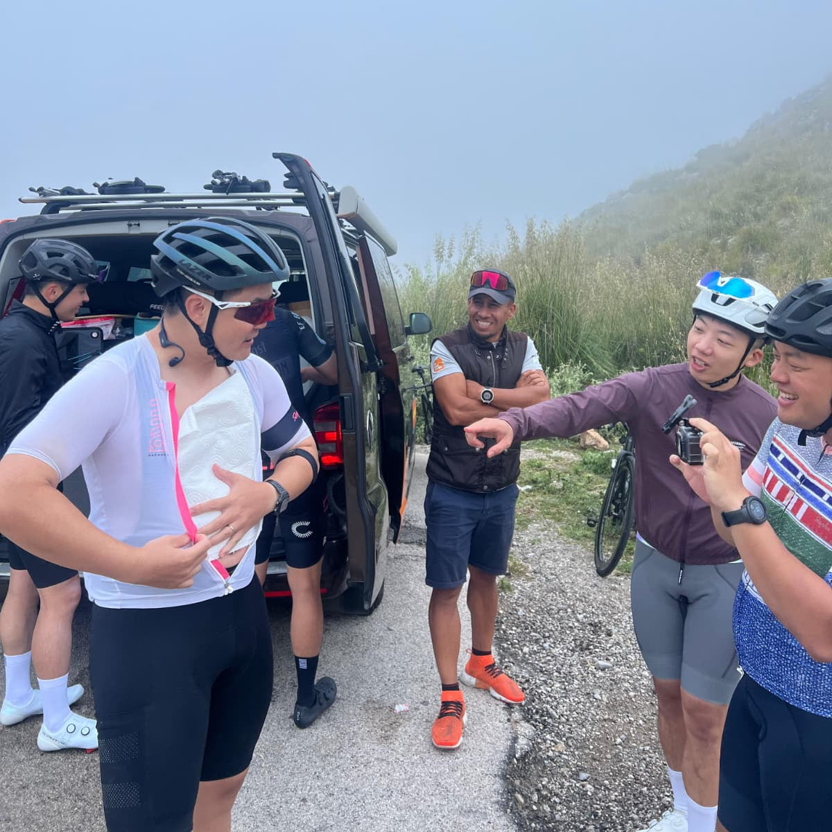 Group of cyclists taking a break by a vehicle on a mountain road
